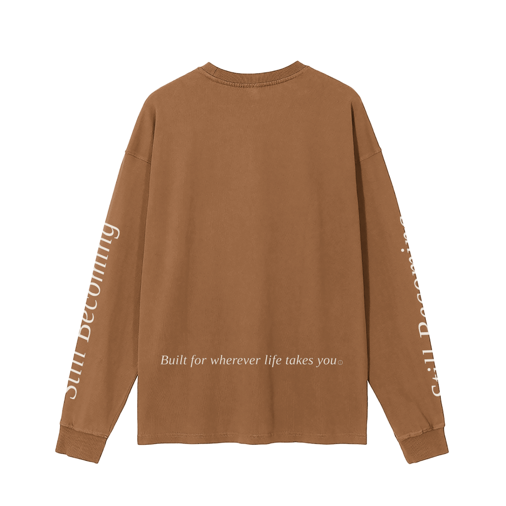The Gatlinburg Long Sleeve T-Shirt is a brown unisex cotton top with "Built for wherever life takes you" on the lower back and "still becoming" in white on both sleeves—a stylish streetwear choice for autumn and winter.