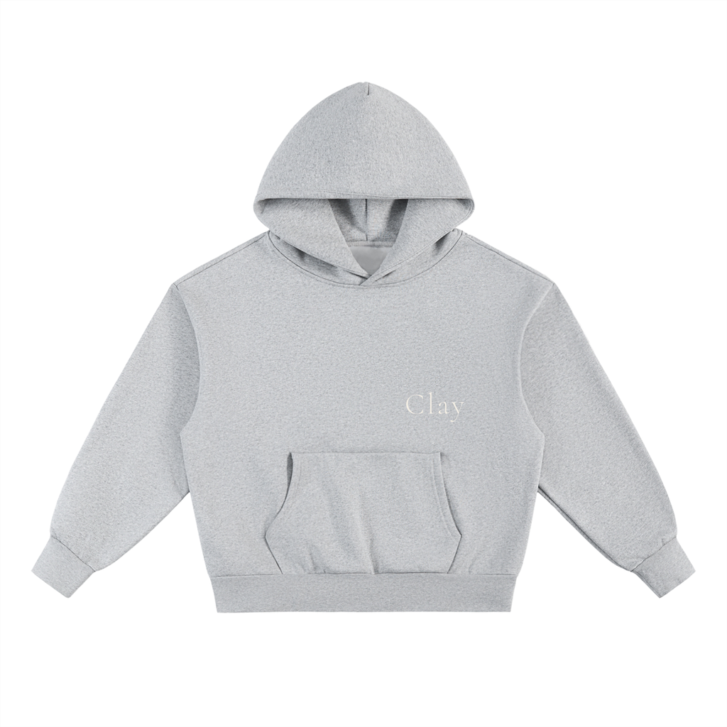 The Selma Hoodie is a light gray, oversized unisex sweatshirt made from a soft cotton blend. It features long sleeves, a front pouch pocket, no visible drawstrings, and "Clay" printed in small white letters on the left chest.