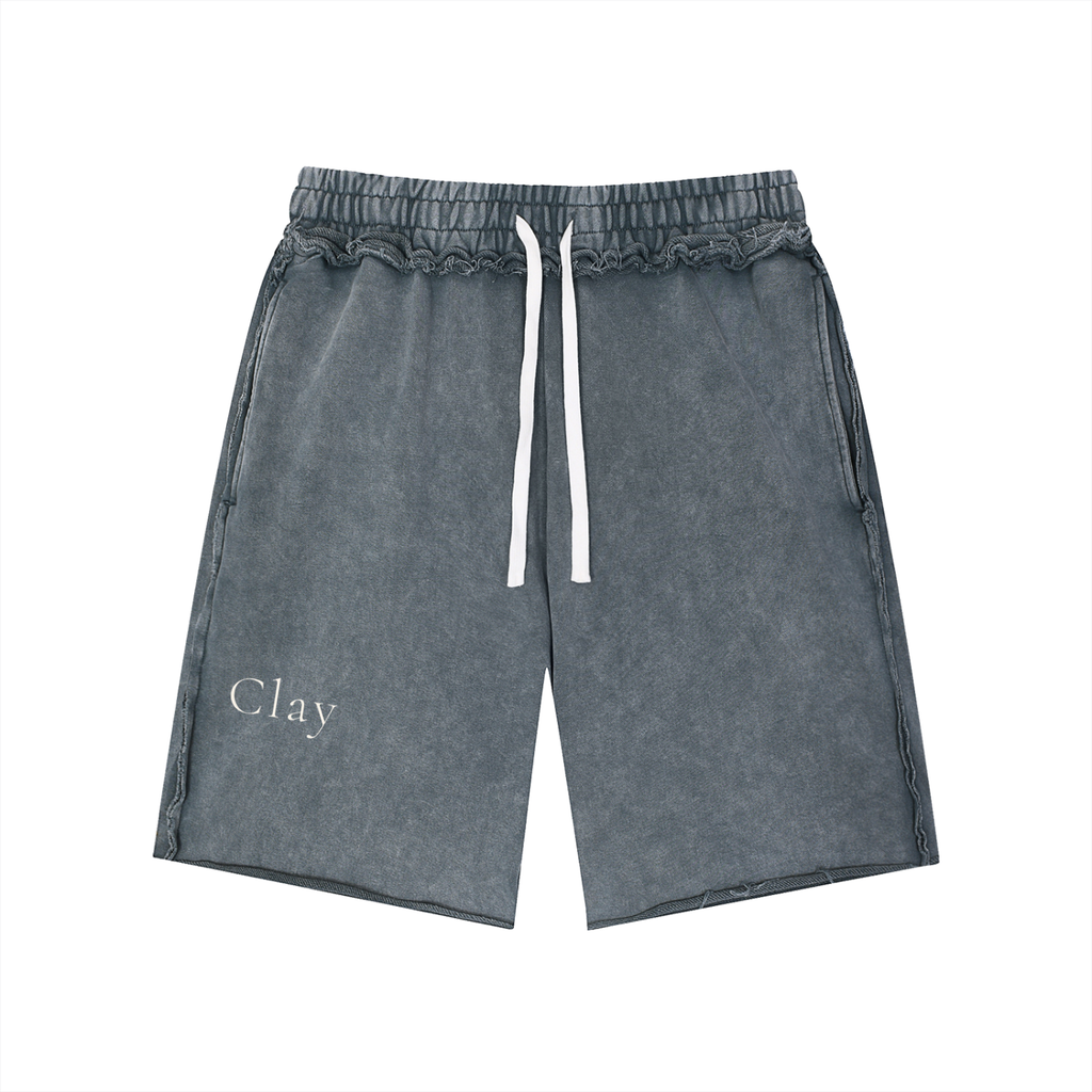 Pensacola Shorts: Gray washed unisex cotton shorts with a loose mid waist, elastic waistband, white drawstrings, and "Clay" printed in white on the left leg. Vintage streetwear style, shown laid flat on a white background.